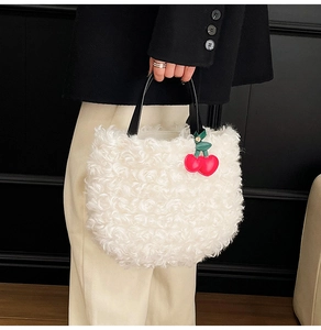 Close-up of white plush bucket bag with black leather handle and red cherry charm