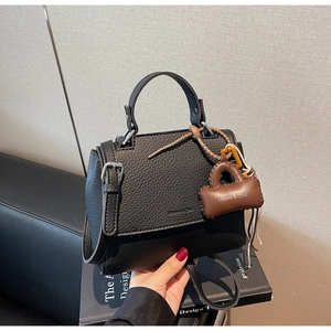 Detail of black lychee grain leather handbag with silver hardware and mini bag charm
