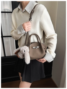 Close-up of brown pebbled leather bucket bag with silver clasp and plush rabbit charm