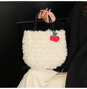 Close-up of white plush bucket bag with black ring handle and cherry pendant detail