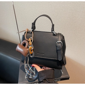 Close-up of black lychee leather square bag with mini bag charm and chain detail