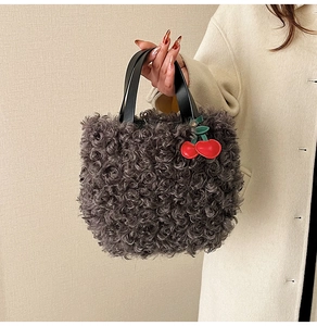 Detail of grey plush faux fur bucket bag with black handle and decorative cherry charm