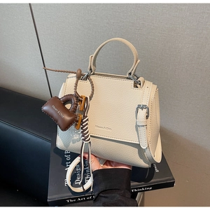 Detail view of beige pebbled leather handbag with Maven & Chic logo and mini bag charm