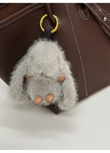 Detail of a fluffy grey rabbit charm with leather limbs on a brown leather handbag