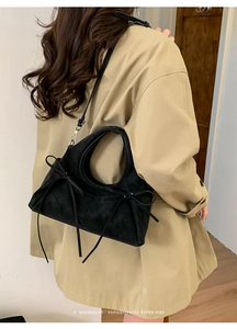 Sac hobo en daim noir avec nœud à franges porté sur un trench-coat de couleur beige