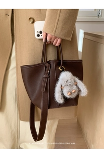 Detail of dark brown leather bucket bag with contrast stitching and rabbit plush charm