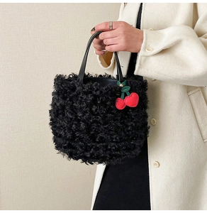 Detail of black faux fur bucket bag featuring slim leather handles and red heart charm
