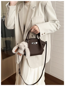 Close-up of deep brown lychee texture leather bucket bag with silver buckle and plush bunny charm