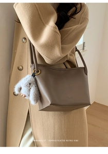 Brown lychee leather bucket bag with cute grey rabbit pendant on model with beige coat