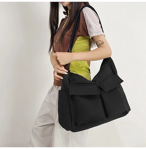 Detail of black large capacity messenger bag with double front flap pockets on model