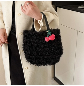 Detail of black plush bucket bag with leather handle and decorative cherry charm