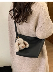 Detail of black pebbled leather bucket bag with plush rabbit charm on beige oversized sweater