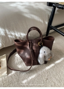 Detail of retro dark brown leather bucket bag with plush rabbit charm on textured carpet