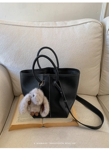 Detail of black pebbled leather bucket bag with white stitching and plush rabbit charm