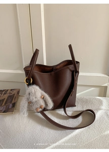 Detail of dark brown pebble leather bucket bag with plush rabbit charm and gold hardware