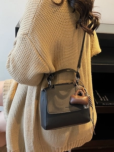 Chic black lychee leather square handbag with a brown tag and beige knit cardigan