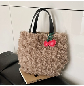 Detail of plush beige bucket bag with black leather handle and red cherry charm accent