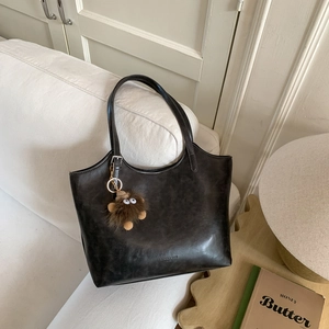 Detalle del bolso bajo el brazo vintage gris con charm de monstruo de pelo en un sofá