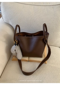 Detail of dark brown pebble leather bucket bag with plush rabbit charm on a sofa