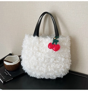 Detail of white plush bucket bag with black leather handle and red cherry charm
