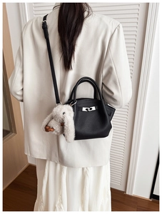 Detail of black lychee leather bucket bag featuring a silver twist lock and plush rabbit charm