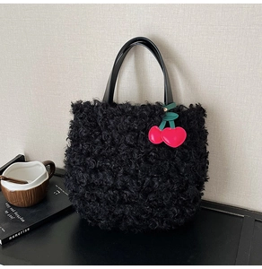 Detail of black sherpa fleece bucket bag featuring a bright red cherry charm accessory