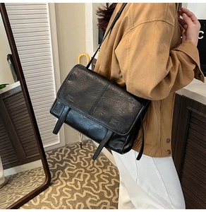 Detail view of a vintage black flap messenger bag with textured pleats and buckles