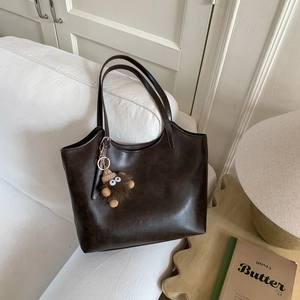 Detalle de bolso tote de cuero marrón oscuro con textura vintage y colgante de peluche