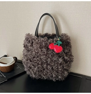Detail of dark grey faux fur bucket bag with black handles and a red cherry charm