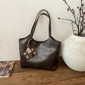 Detalle de bolso tote retro marrón oscuro con amuleto de peluche y texto en relieve