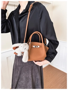 Detail of caramel leather bucket bag with silver lock and plush bunny charm on shoulder