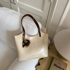 Detalle de bolso tote blanco crema con correas marrones y colgante de peluche