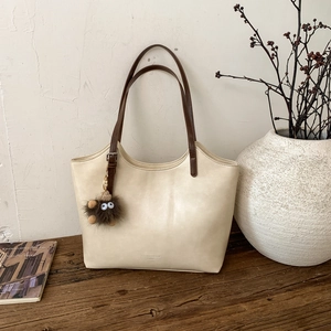 Detalle de bolso tote de cuero crema con asas marrones y colgante en banco de madera