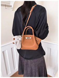 Detailed view of brown lychee grain leather bucket bag with silver turn-lock and elephant charm