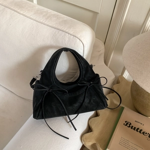 Détail d'un sac à main en daim noir avec nœuds et boucles argentées sur un canapé blanc
