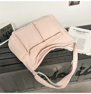 Detail of light pink quilted tote bag with dual front pockets on industrial bench