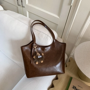 Detalle de bolso tote marrón oscuro en cuero sintético con colgante en sofá blanco