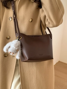 Deep brown lychee leather crossbody bucket bag with grey plush bunny charm on model