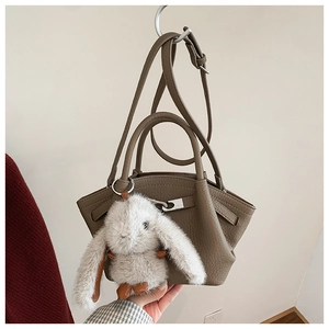 Close-up of textured leather winged bag with metal buckle and plush rabbit charm