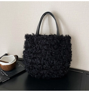 Detail view of black faux shearling bucket bag with glossy rounded handles on a table