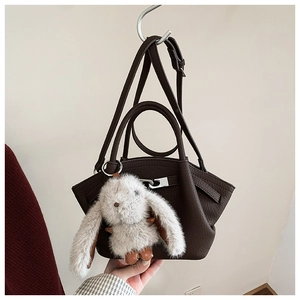 Detail of dark brown leather bucket bag with silver buckle and cute plush rabbit charm