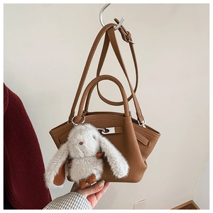 Detail of a brown lychee pattern leather bucket bag with a cute white rabbit plush charm