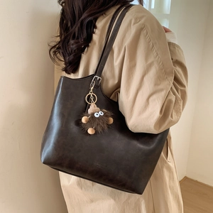 Detalle de bolso tote grande de cuero marrón oscuro con correa ajustable y colgante peluche