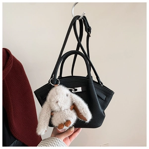 Detail of black pebbled leather bucket bag with silver buckle and white plush bunny charm