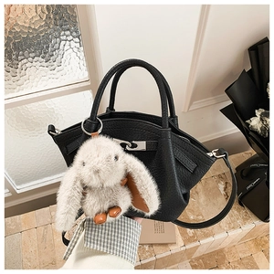 Detail of black lychee leather bucket bag with metal buckle and plush bunny charm