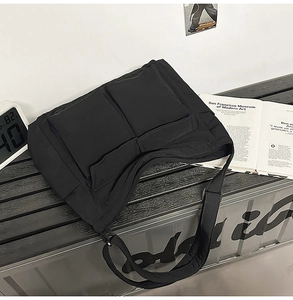 Close-up of black utility messenger bag with dual front flap pockets and adjustable strap