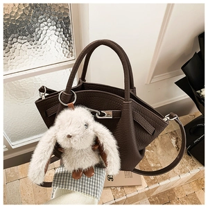 Detail of dark brown leather bucket bag featuring a silver lock and white rabbit plush charm