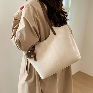 Detalle de un bolso tote beige con correas marrones y colgante de peluche sobre un gabán