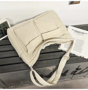 Close-up of beige quilted nylon tote bag with dual front pockets and wide shoulder strap