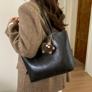 Detalle de bolso tote de cuero sintético negro con amuleto de monstruo sobre blazer marrón